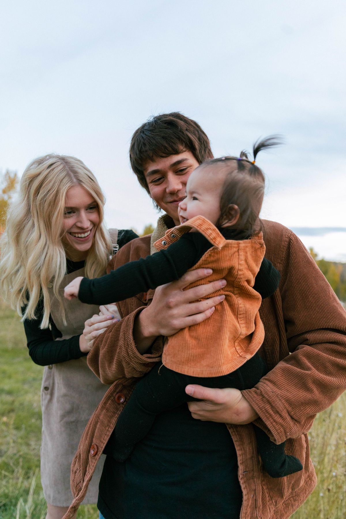 Parents holding their baby together in a field
