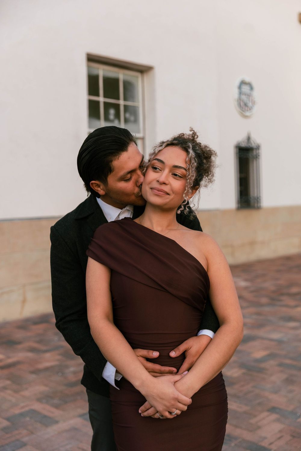 A formally dressed couple embracing outside an arched building
